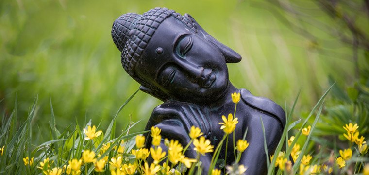 Black Buddha statue in garden with flowers By Nicky Rhodes